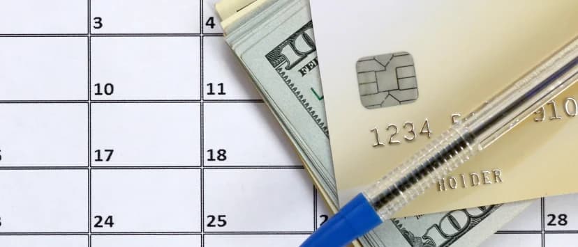 Calendar, pen and bank card on a desk with money in the background