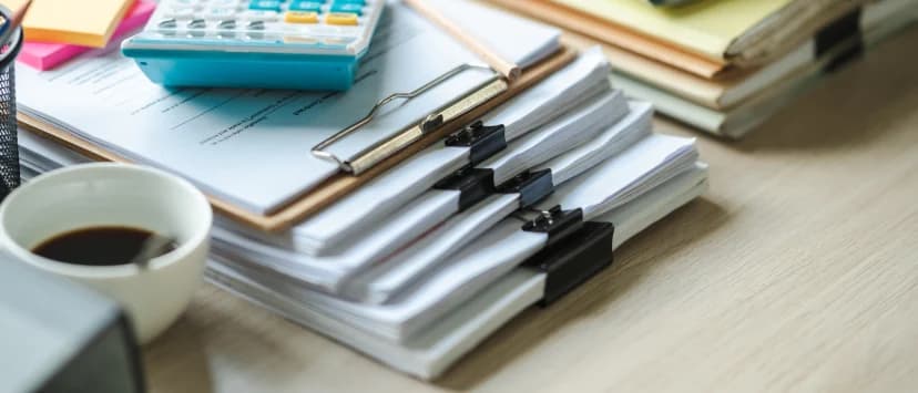 Stacks of documents, a clipboard and calculator on a desk